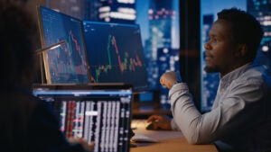 Investment manager working in office in front of computer with stock market charts visible on displays