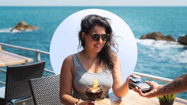 A young woman with sunglasses dining oceanside paying her server with a credit card