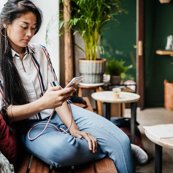 A cafe customer sitting by the window in her favorite cafe, using her smartphone and relaxing.