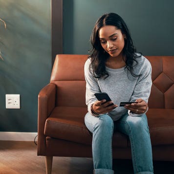 woman sitting on her couch and looking at her phone and credit card