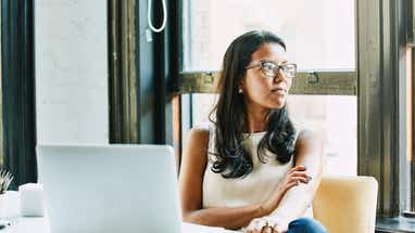 Woman sitting at a table with a laptop in front of her, but she's looking to the right of the photo.