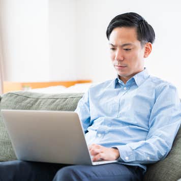Man sitting on a couch looks at a laptop.