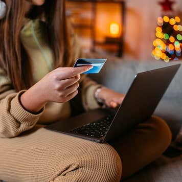A woman holds a credit card and online shops with holiday lights in the background