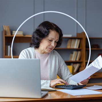 Older woman sitting at her kitchen table with a laptop and looking at her policy