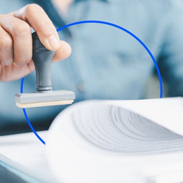 A hand applies a stamp to a document.