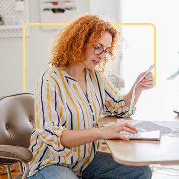 Red haired woman reading bill at desk.