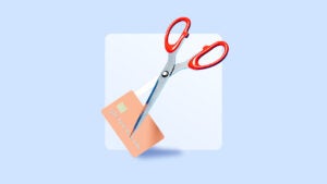 A peach-colored credit card being cut by a pair of scissors with red handles on a blue background.
