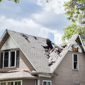 Clear sky after a storm with a house in the foreground. The roof has been severely damaged in the picture.