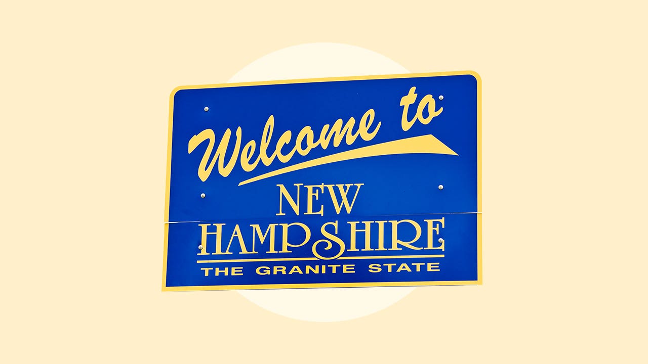 A blue sign with gold lettering saying "Welcome to New Hampshire The Granite State"