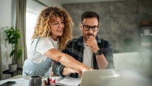 hoto of a young couple working from home together, sitting in the working area of ​​the living room of their modern apartment, surrounded by laptops, notebooks and cups of coffee