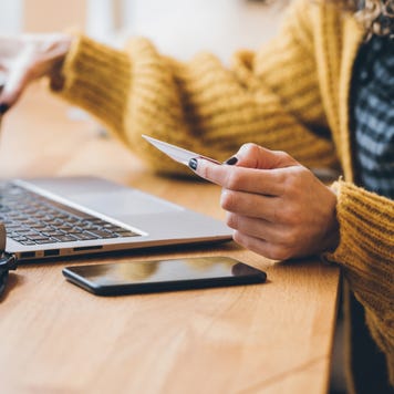 Close-up view of a person leaning over a desk at a laptop and holding a credit card.