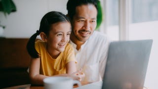 Man and child sitting at table smiling at laptop.
