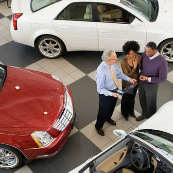 A Black couple talk to a salesperson at a car dealership.