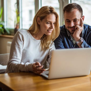 Couple sitting at kitchen table using laptop