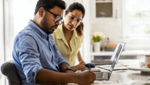A couple works on their finances on a laptop in their kitchen.