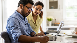A couple works on their finances on a laptop in their kitchen.