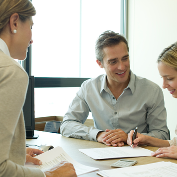 A couple signs papers across the desk from a loan agent.