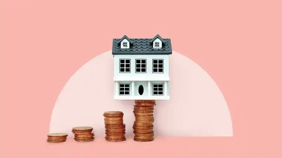 house balanced on stack of coins, pink background, photo illustration